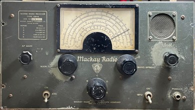 Gray tabletop receiver with a semi-circular dial, 5 knobs. 2 toggle switches and a small speaker